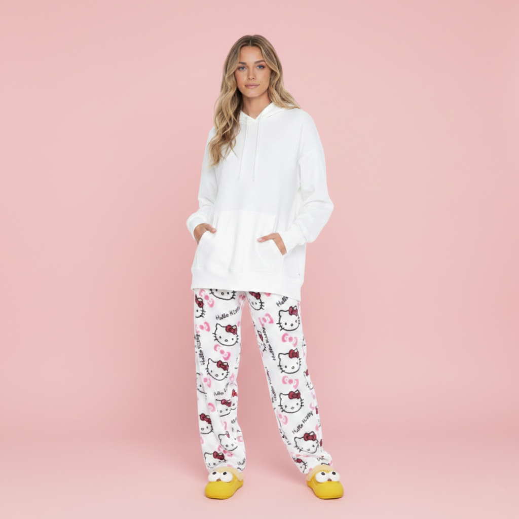 Woman wearing a white hoodie and Hello Kitty pajama pants on a pink background